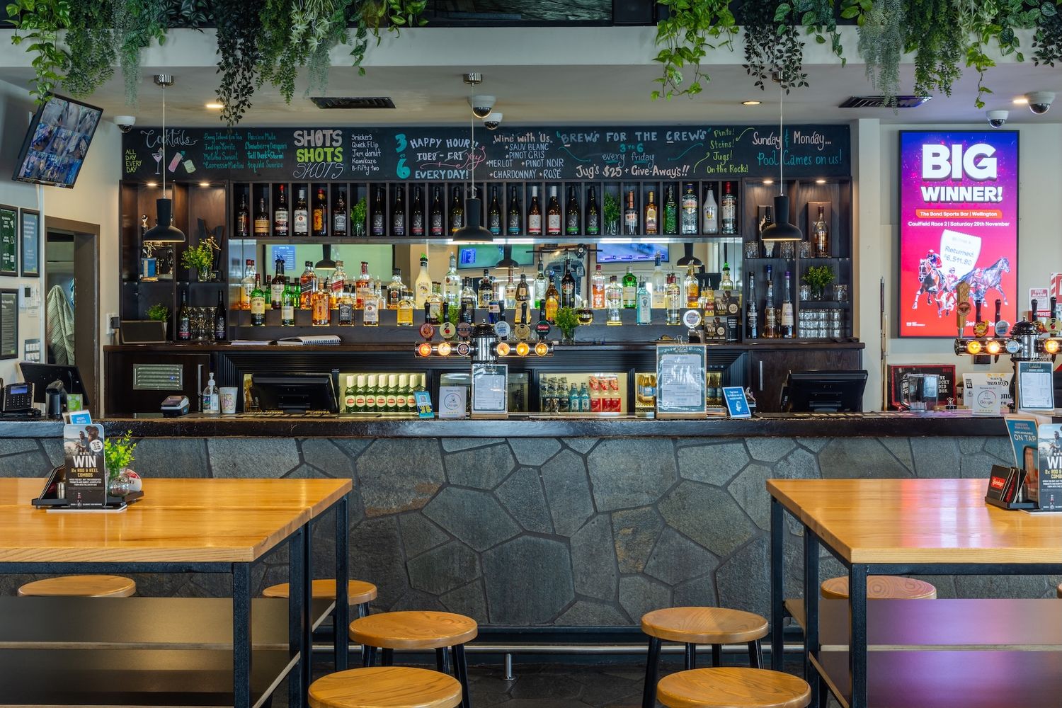 Long wooden bar counter with high stools and extensive liquor display in modern pub setting.