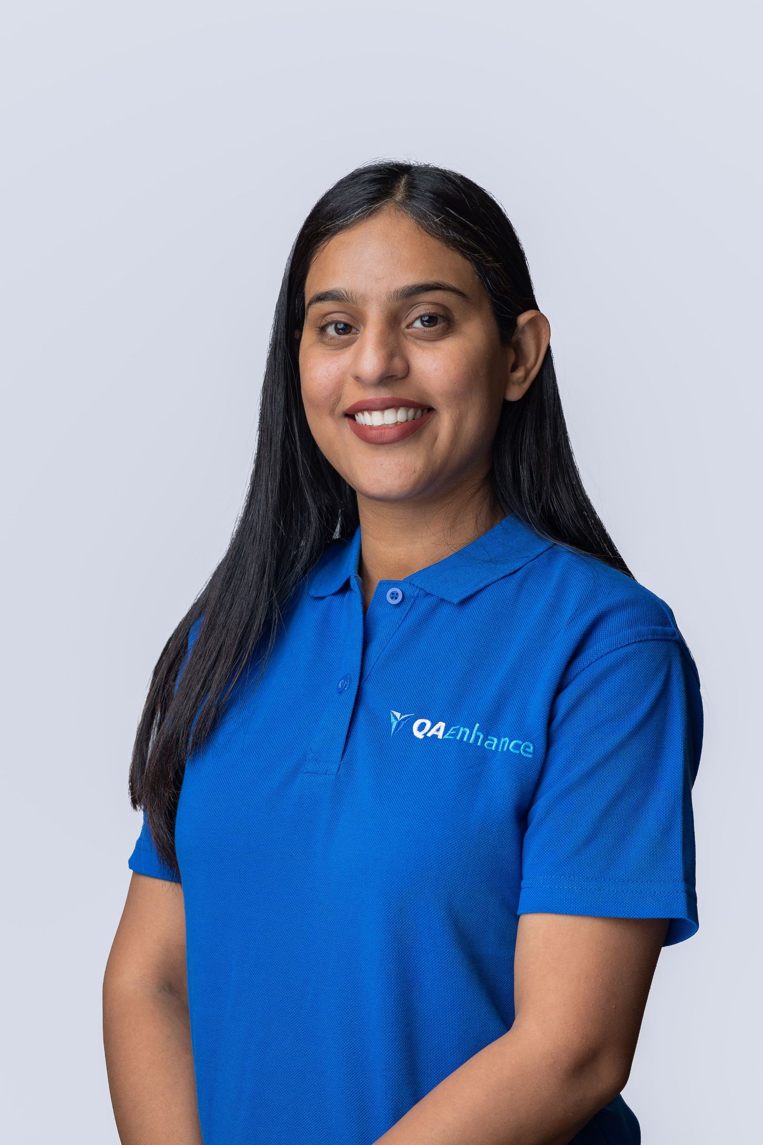 Woman in blue QAenhance polo shirt smiling professionally against light gray background.