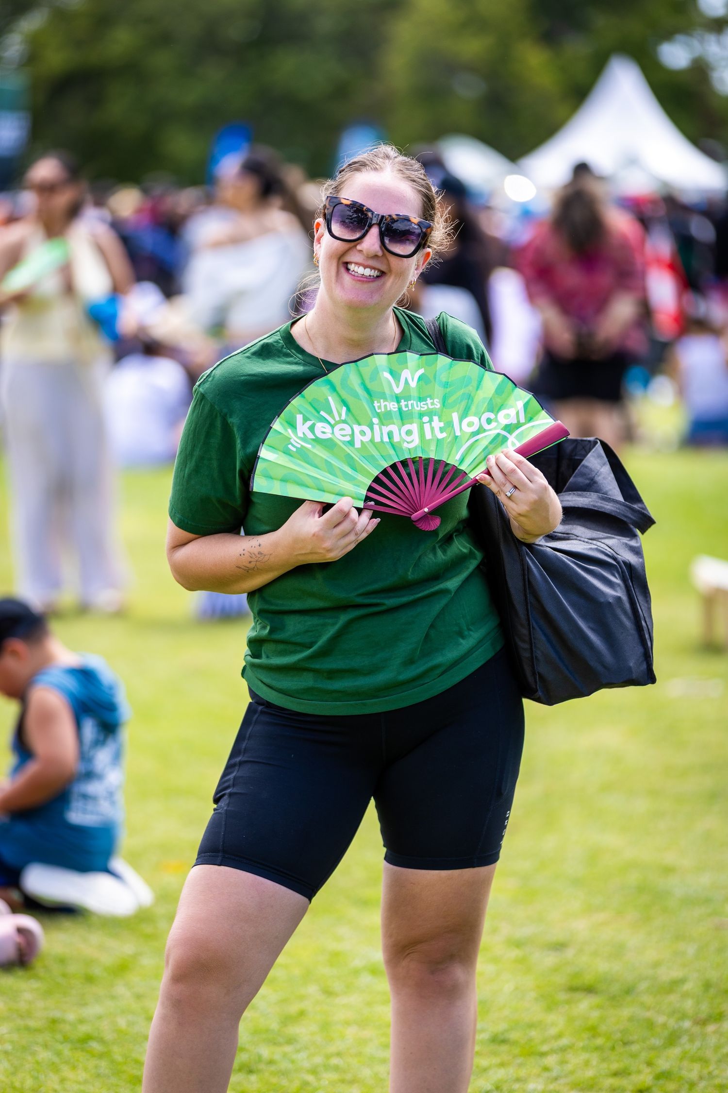 Staff member in green shirt holding fan while working at outdoor community event.