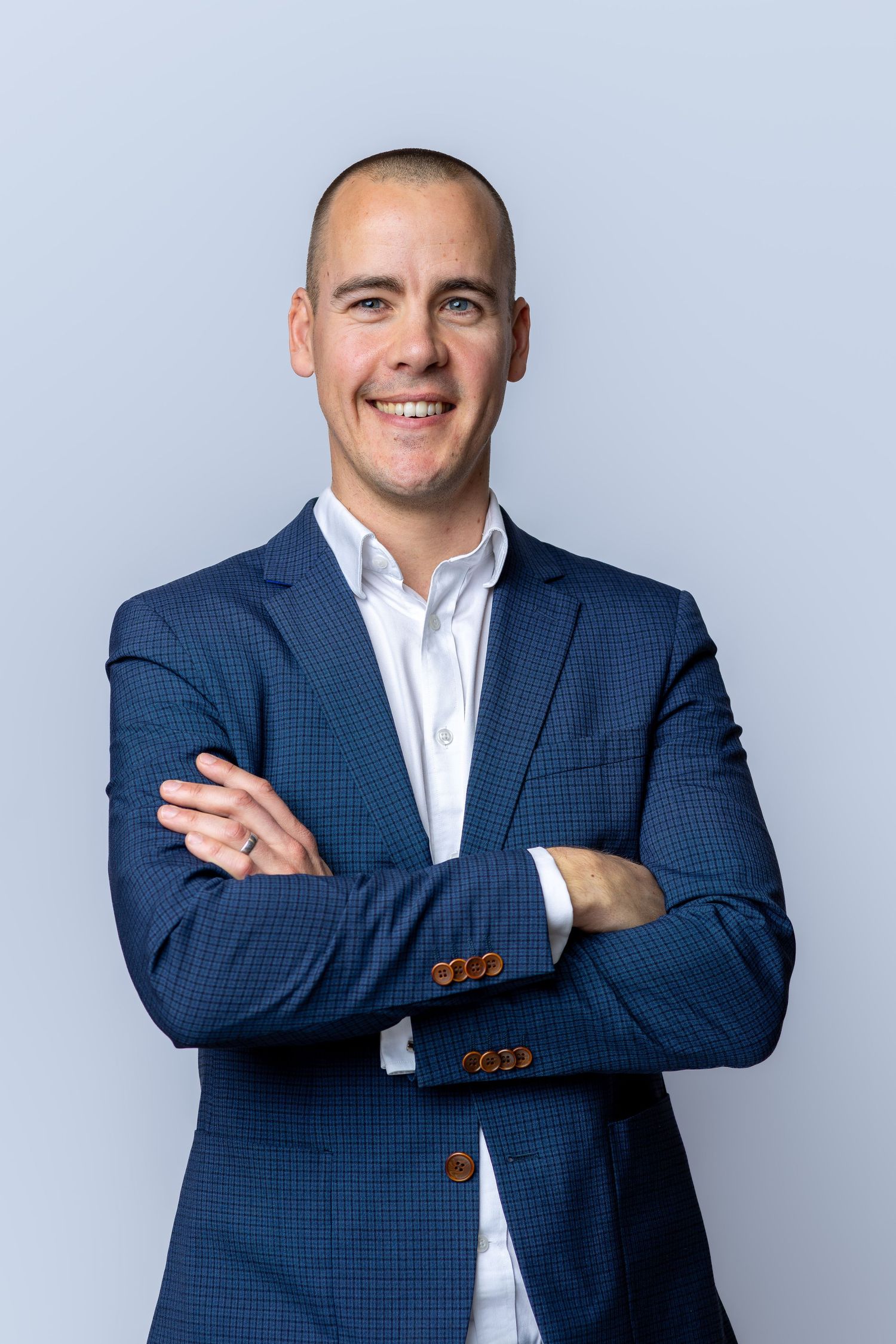 Professional man in navy blazer smiling with arms crossed against light blue background.