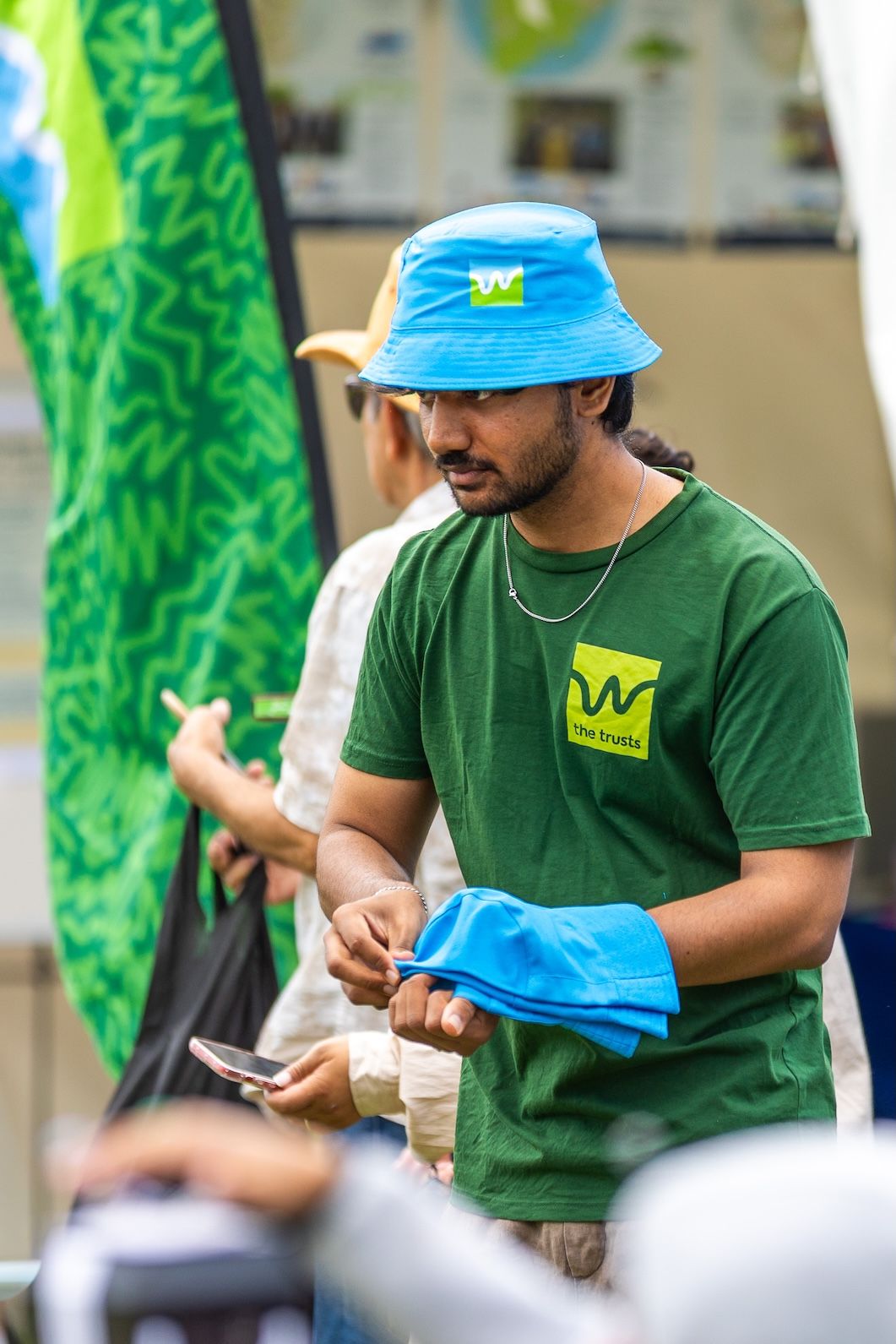 Staff members in green shirts with blue hats handling materials at outdoor event.