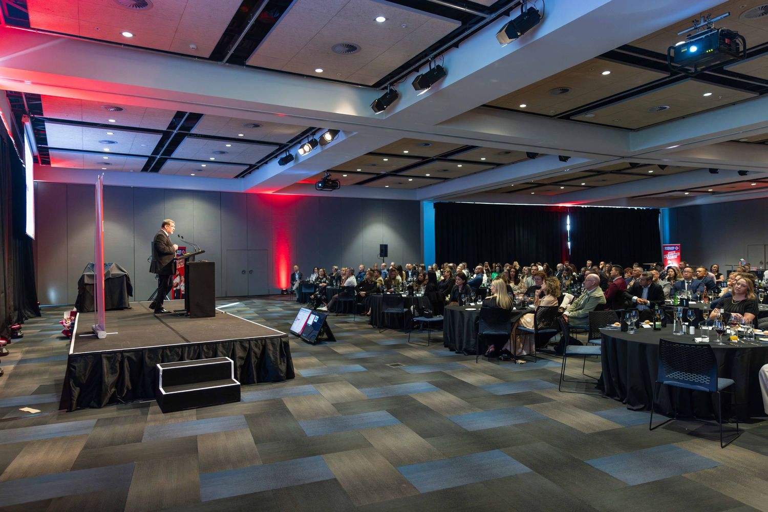 Large conference room setup with rows of chairs and stage lighting for a corporate event.