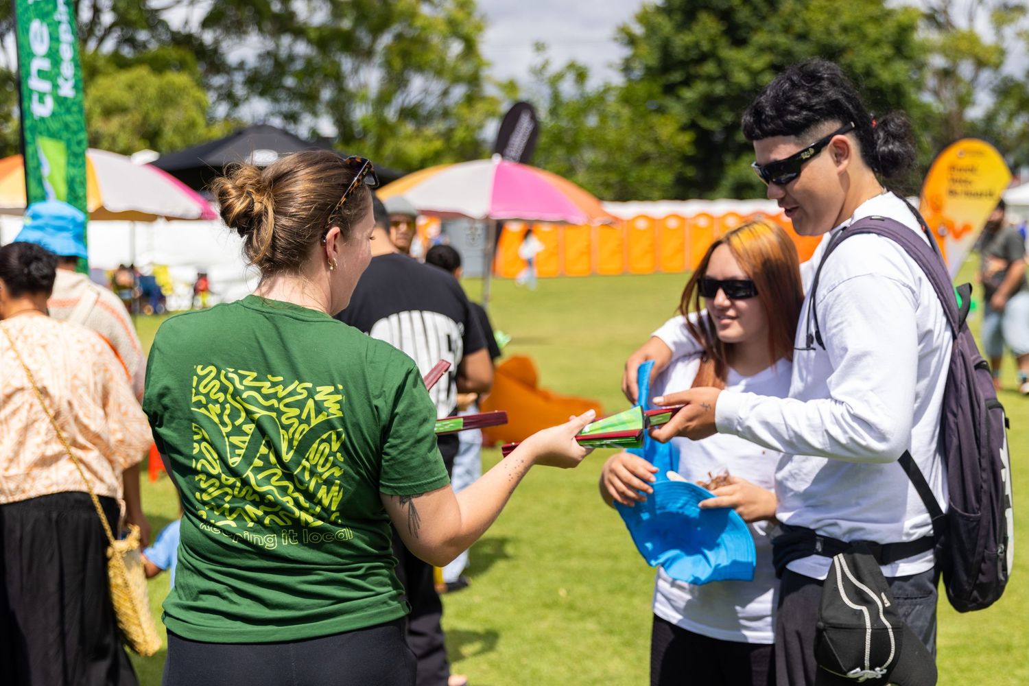 Crowd enjoying outdoor festival activities on grassy field with tents and banners.