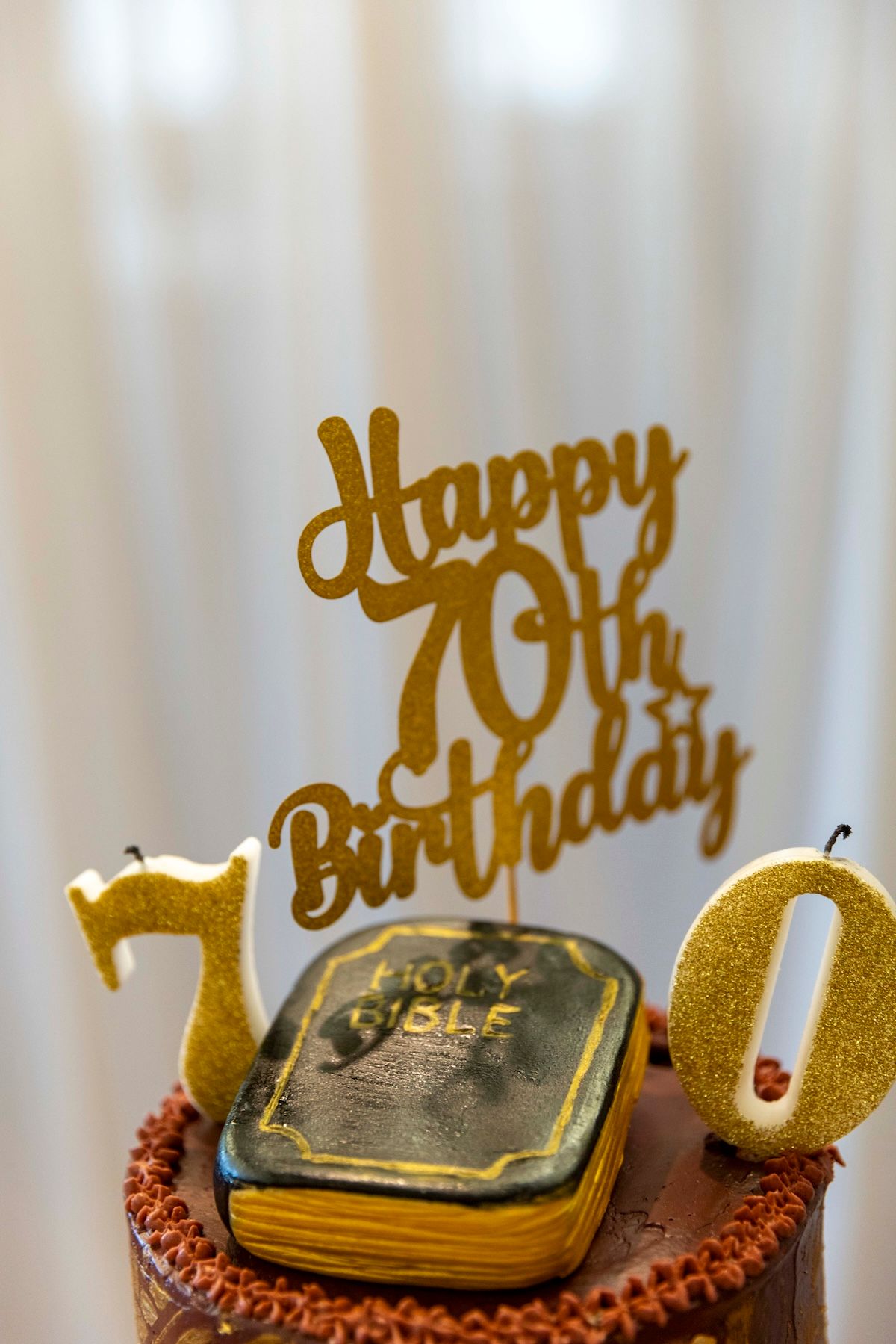 Gold 70th birthday cake topper with numbers and a vintage holy bible decoration on chocolate frosted cake.
