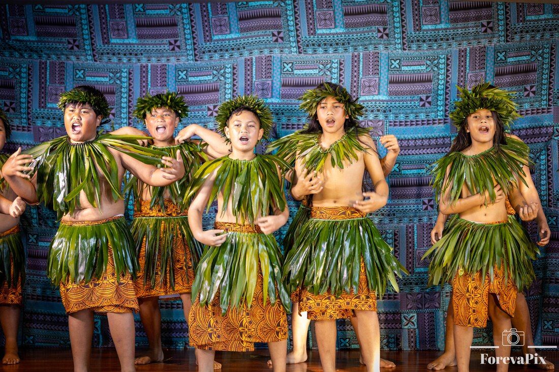 Young performers in traditional Polynesian grass skirts and leaf headdresses dancing on stage at a cultural festival.