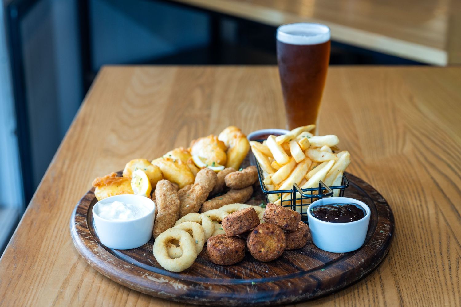 Restaurant table setting with wooden platters featuring pub food and beer glasses.