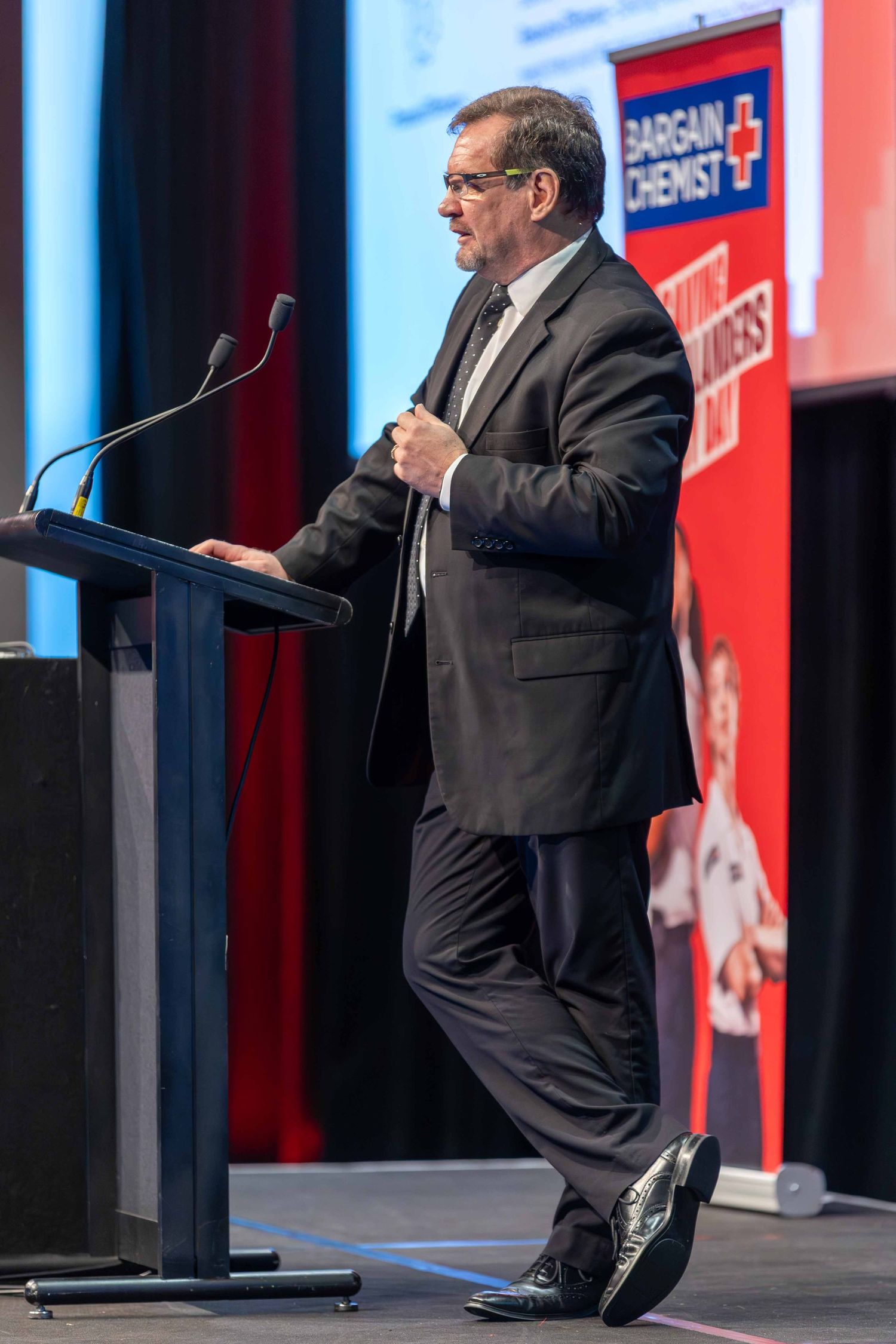 Business presenter gesturing while speaking at podium during corporate event.