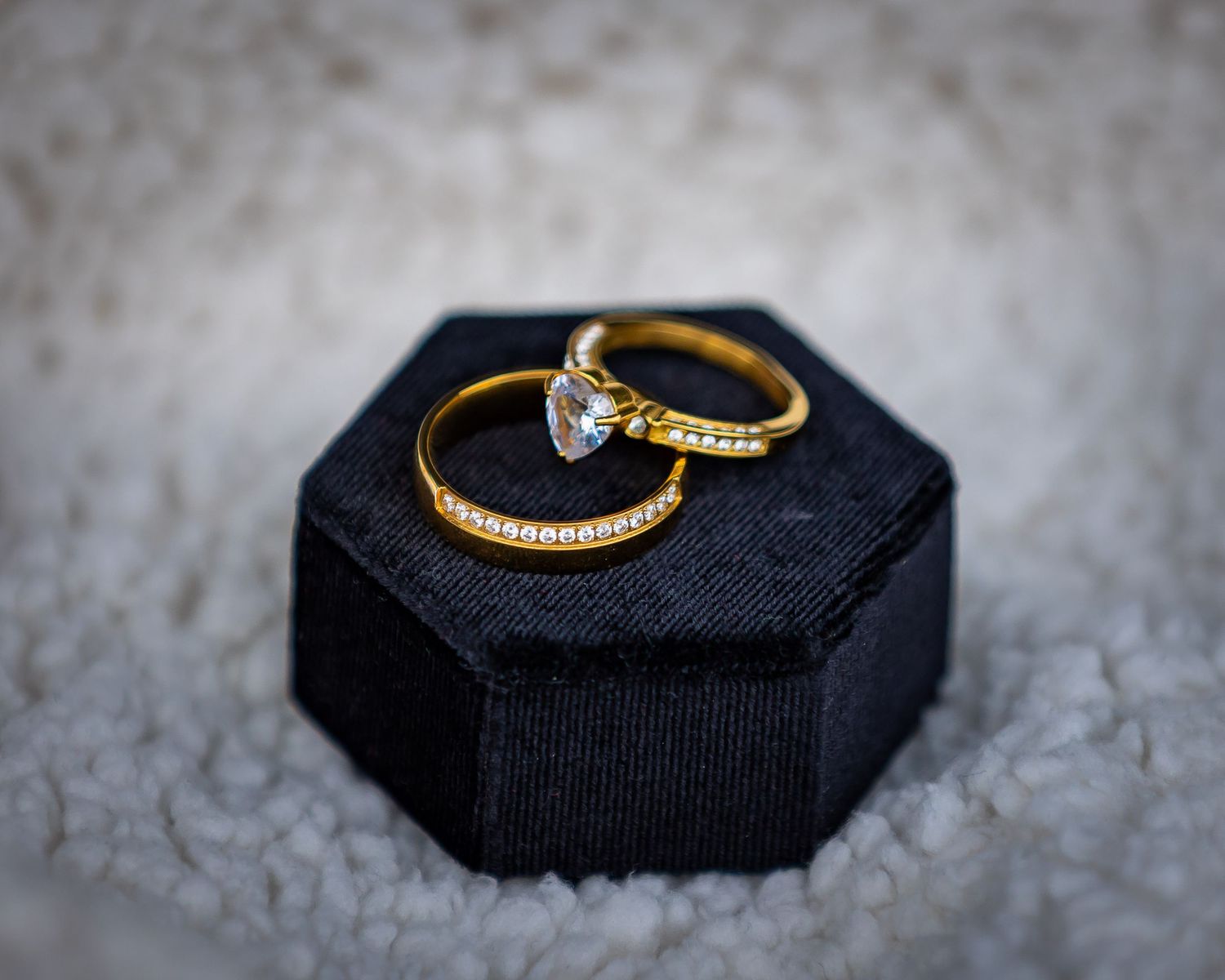 Two gold diamond rings displayed in a black velvet hexagonal ring box on a textured white surface.
