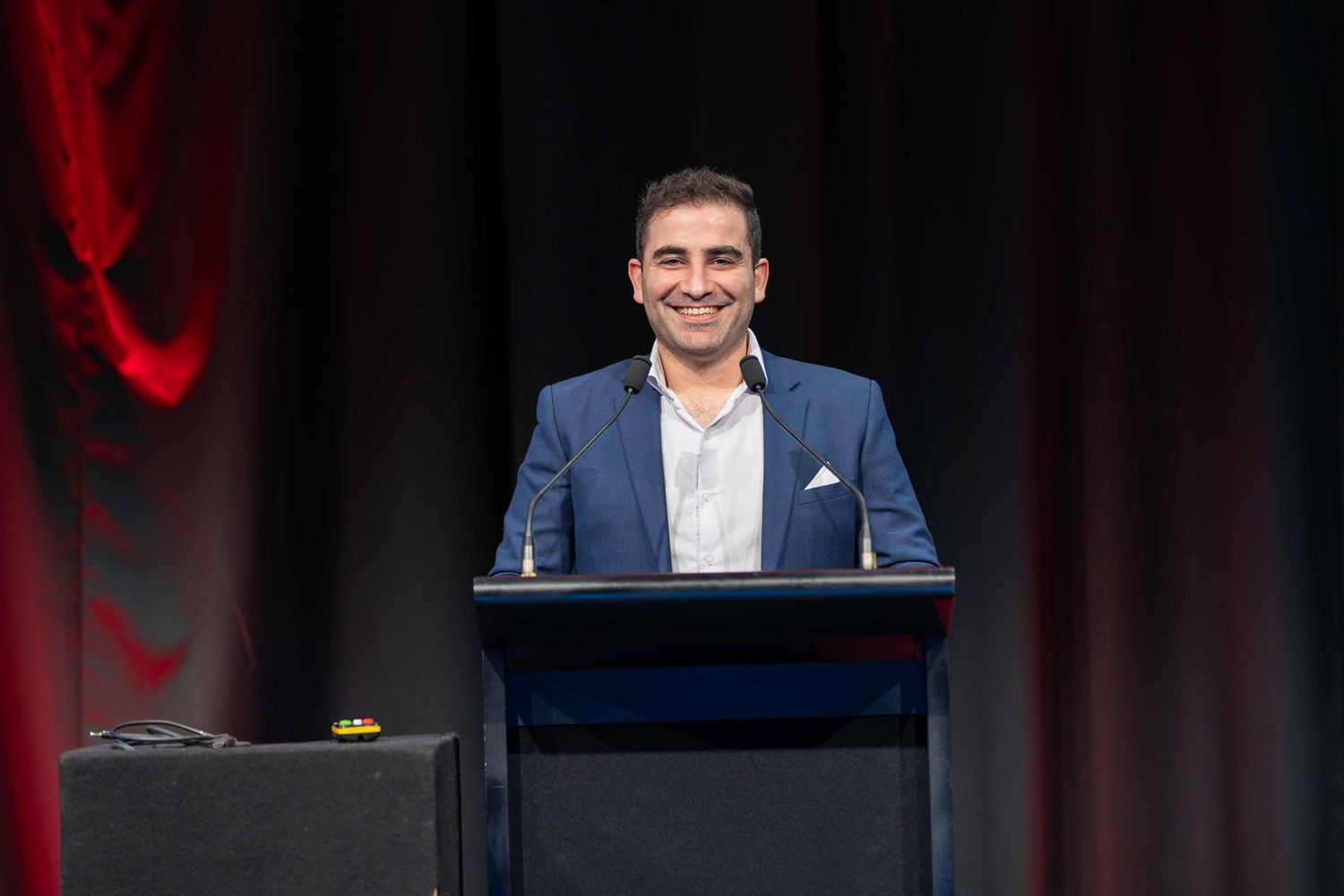 Speaker presenting at a podium during an event with dark curtain backdrop.