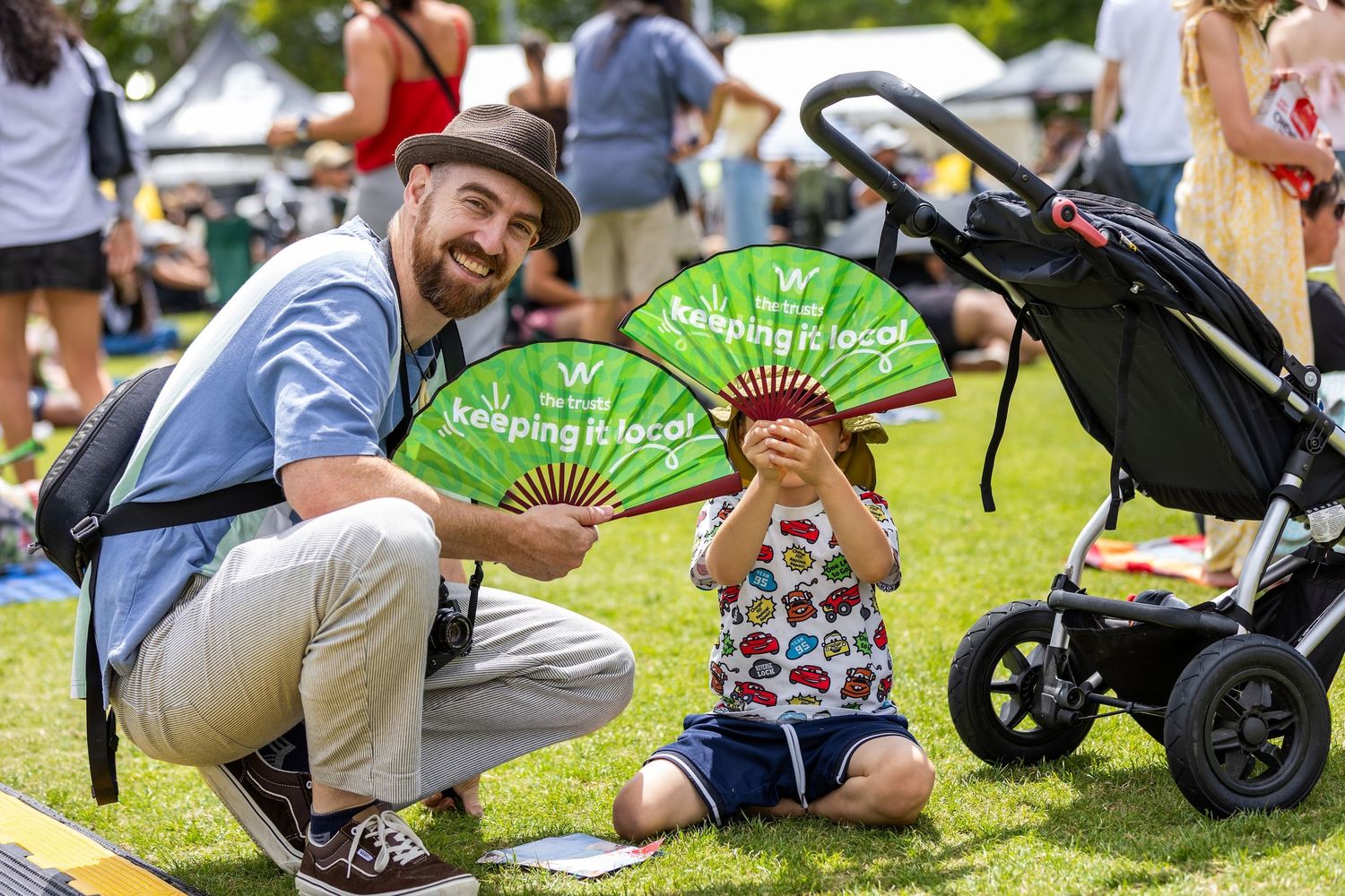Festival attendees sitting casually on lawn with strollers and green fans.