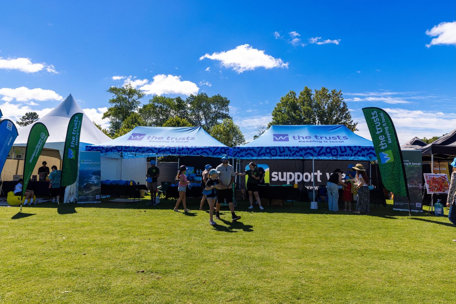 Promotional event tents with support banners and green feather flags on grass field.