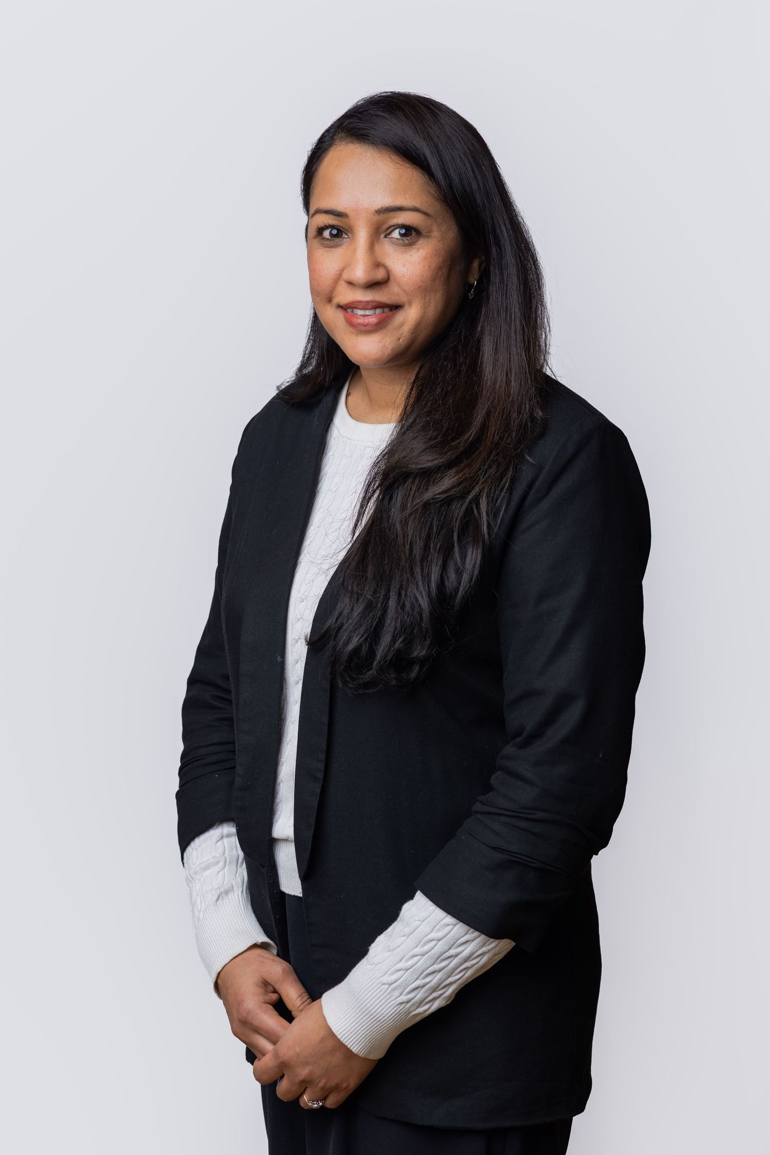 Professional woman in black blazer and white top smiling confidently against a light gray background.