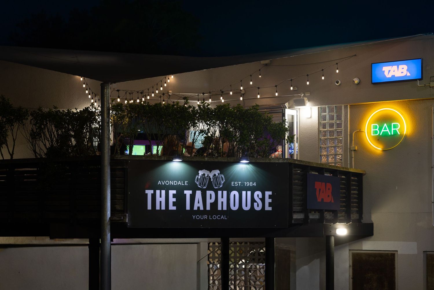 Exterior night view of The Taphouse bar signage with ambient lighting.
