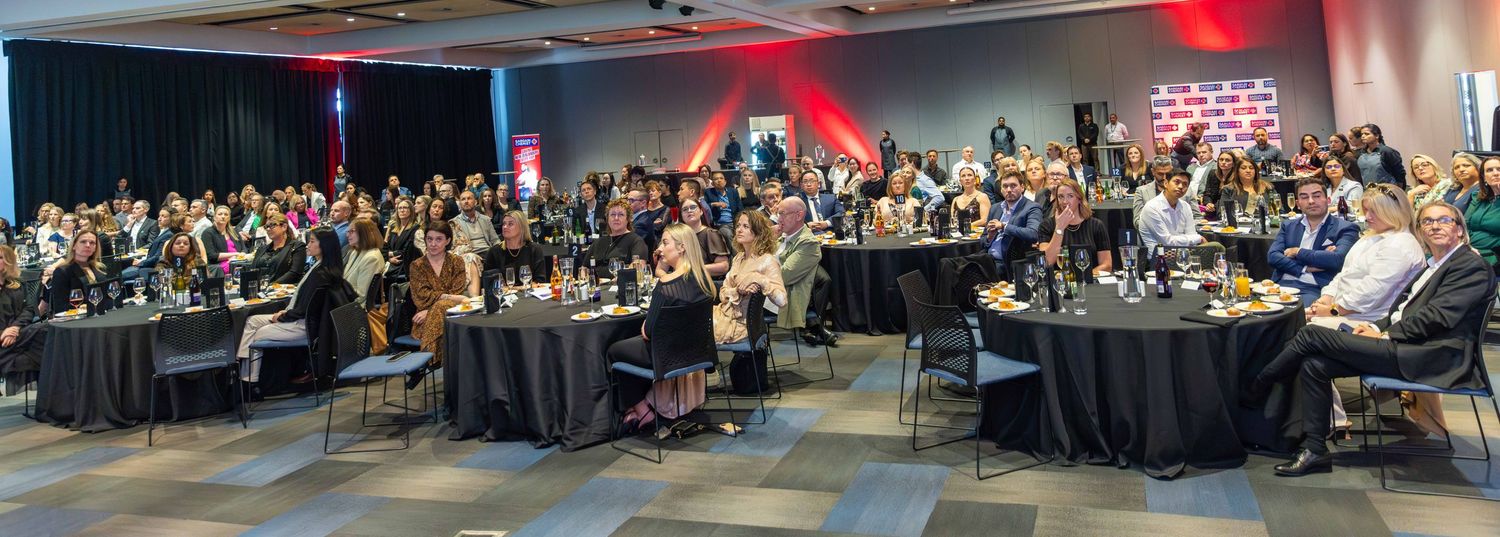 Large corporate conference audience seated at round tables in a modern venue.