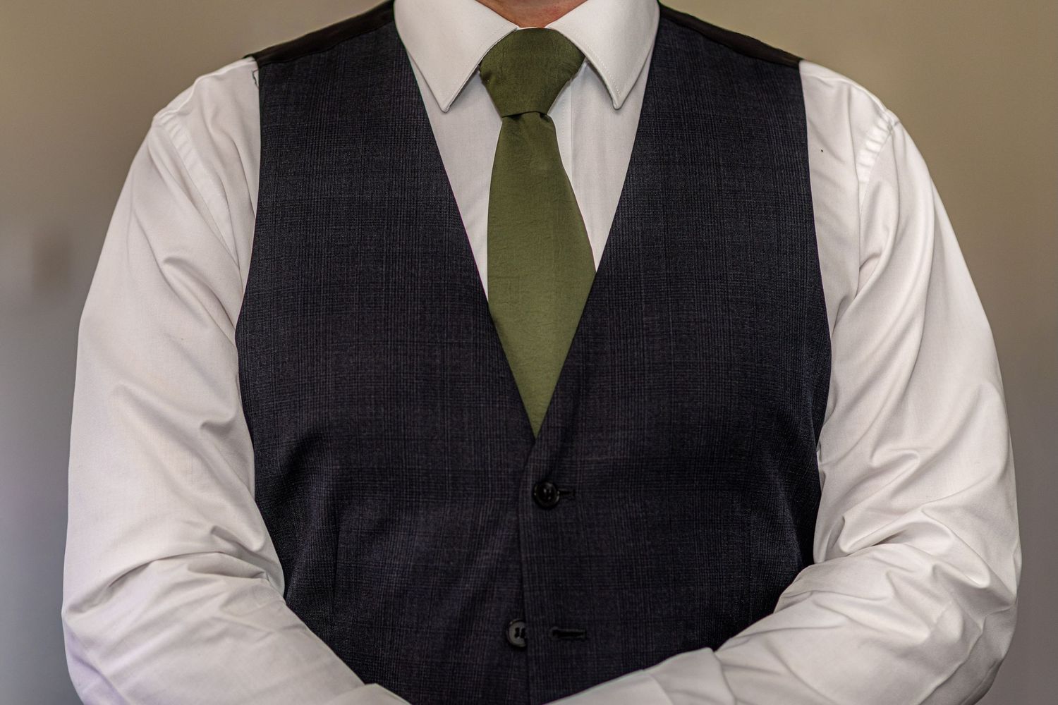 Man wearing a dark charcoal suit vest with a green tie and white dress shirt, arms crossed.