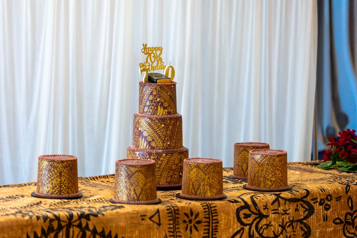 Elegant gold wedding cake with intricate black designs displayed on a white tablecloth at a reception venue.