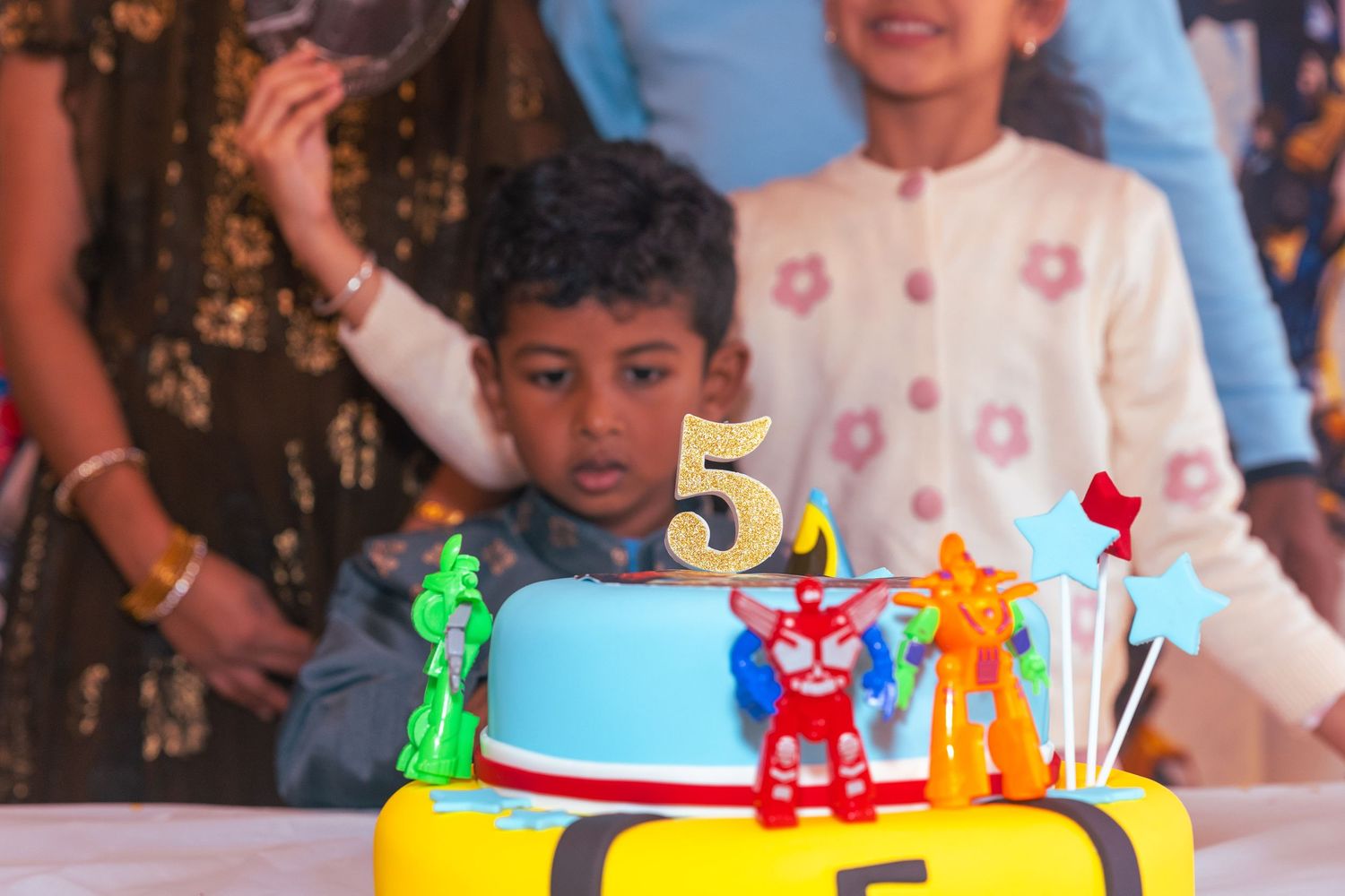 A young boy celebrates his 5th birthday with a colorful cake topped with toy figures and a number 5 candle.