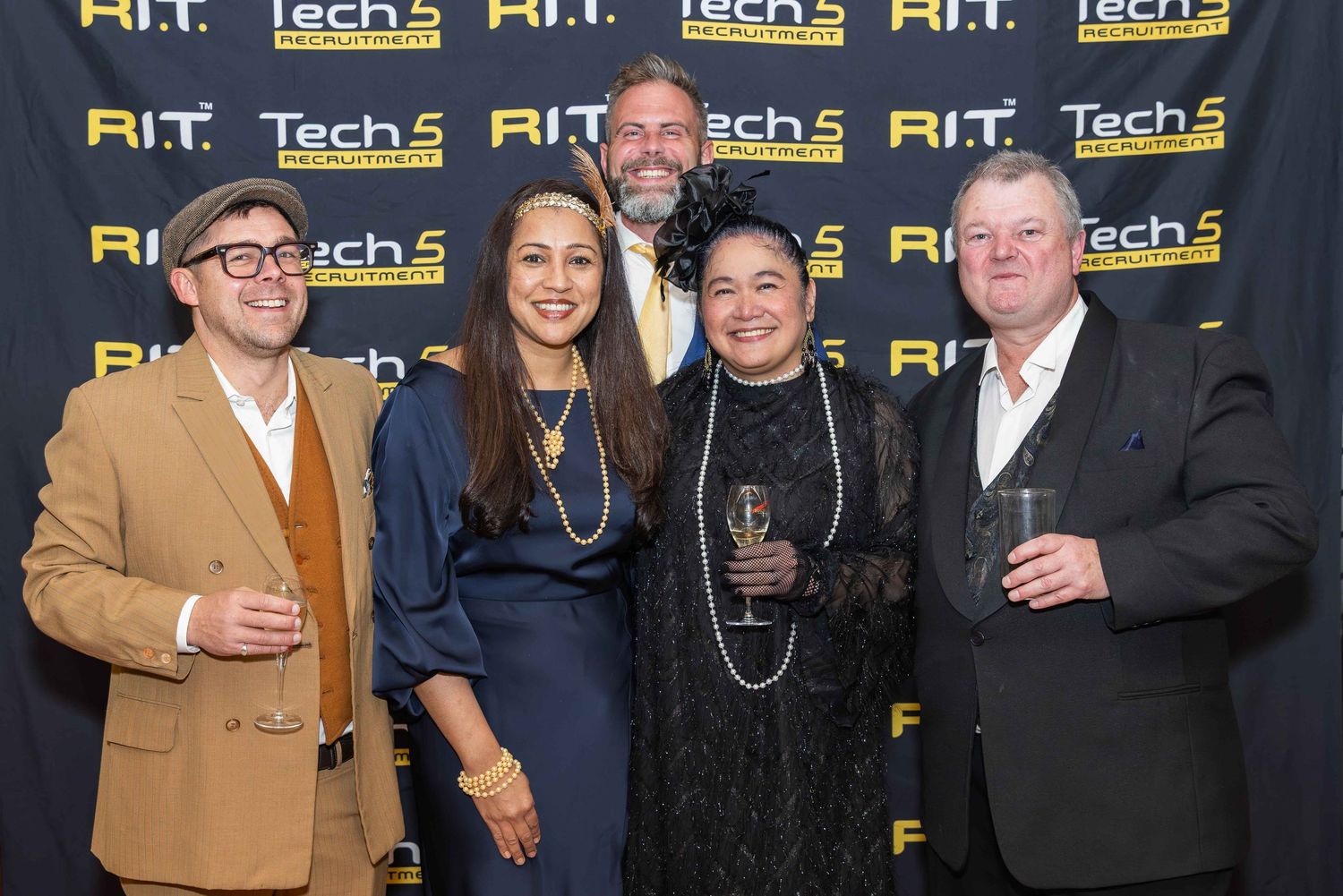 Five people posing together at RIT Tech5 awards event, smiling in front of branded yellow and black backdrop.