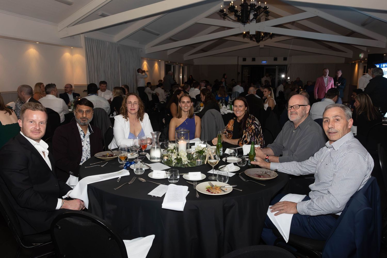 Group of professionals seated at a round table during a formal dinner event in an elegant banquet hall.
