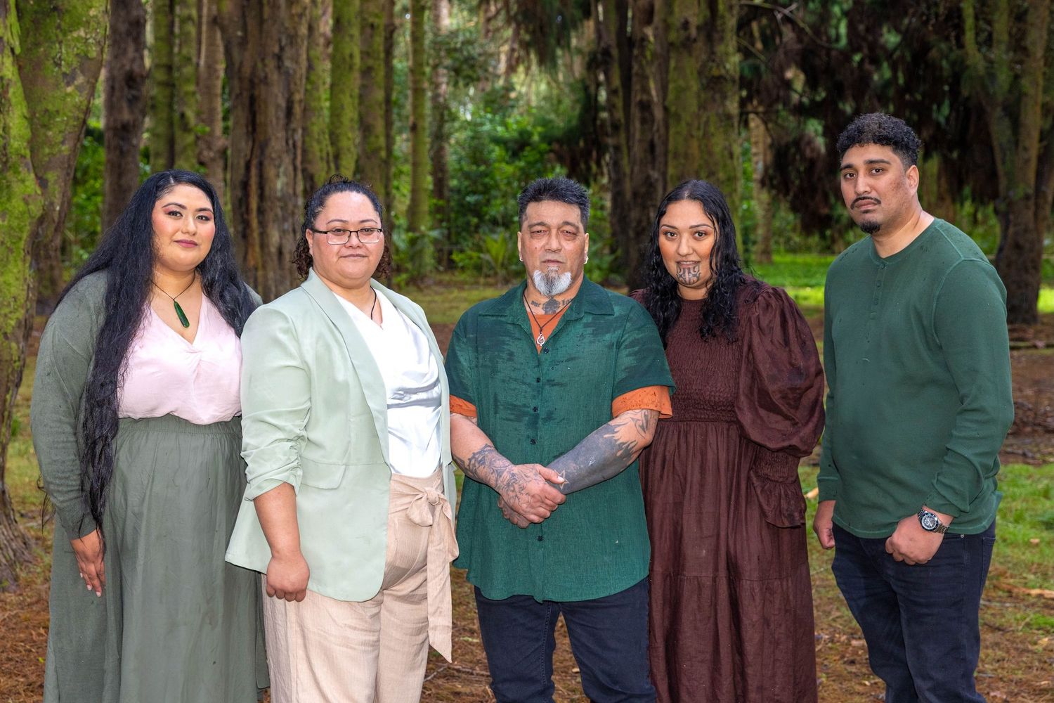 Five people posing together outdoors among tall trees in a lush green forest setting.