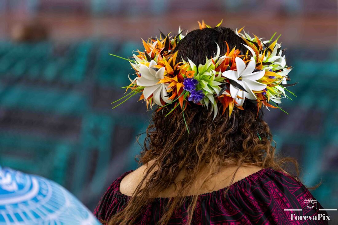 Woman with long curly hair wearing a vibrant tropical flower crown with white, orange, and purple blooms.