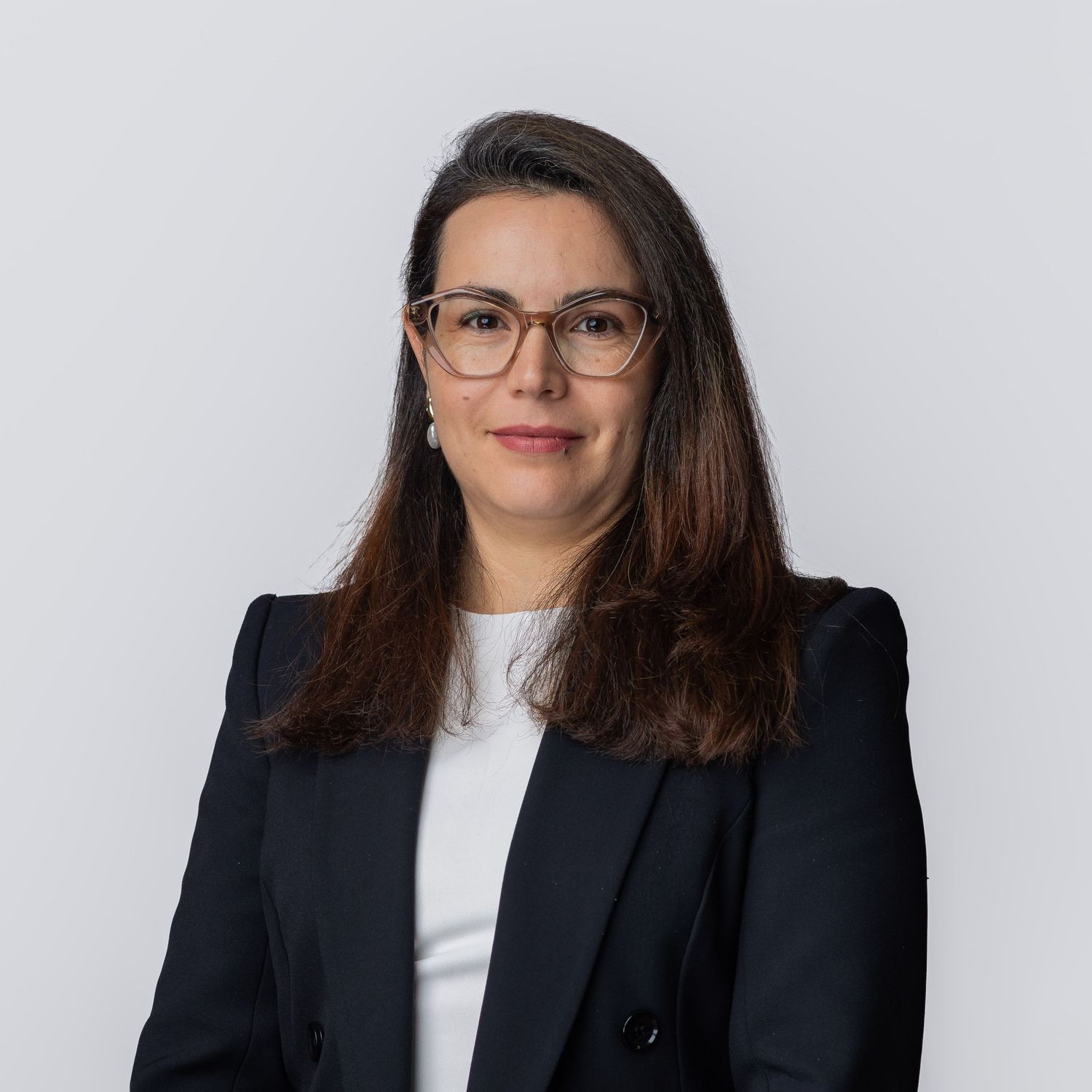 Professional woman in dark blazer and glasses with brown hair poses for a corporate headshot photo.
