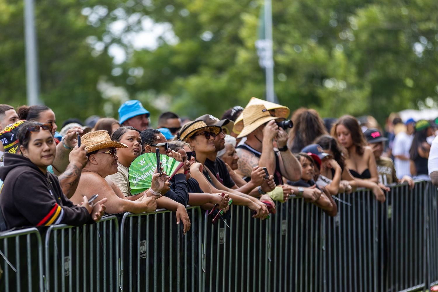 Large crowd standing behind metal barriers at outdoor festival event.