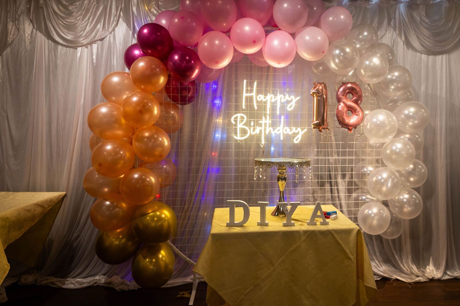Colorful 18th birthday party decoration with pink balloon arch, neon Happy Birthday sign, and gold DIVA table display.