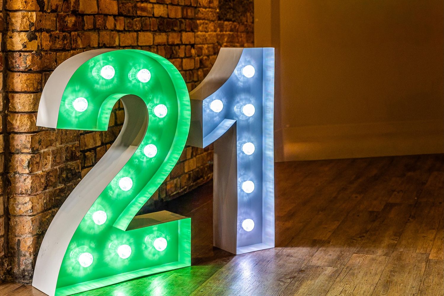 Illuminated marquee number 21 light-up letters in green and white with bulbs, displayed against a brick wall.