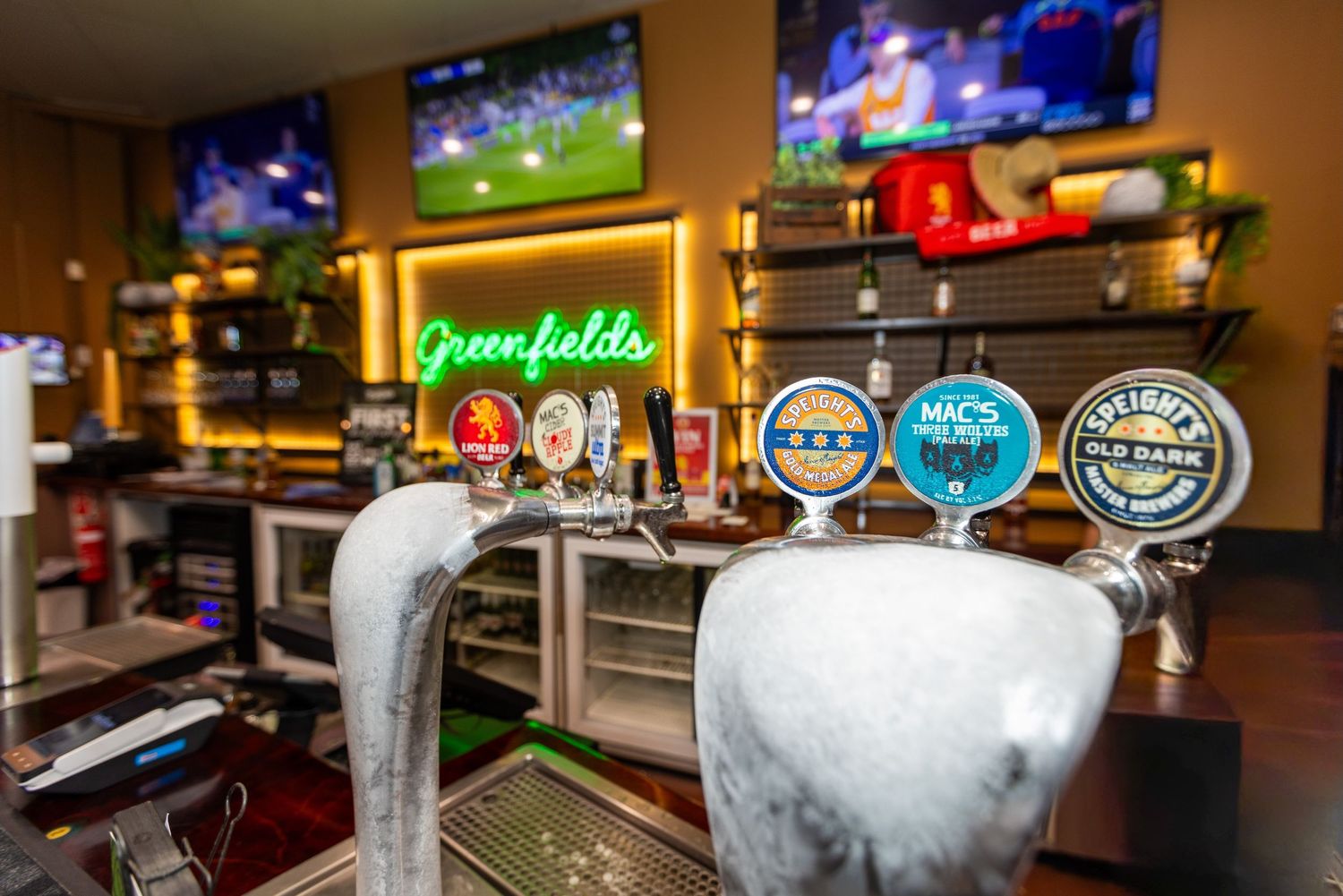 Beer taps and TV screens at a sports bar showing multiple games with frosted draft handles in the foreground.