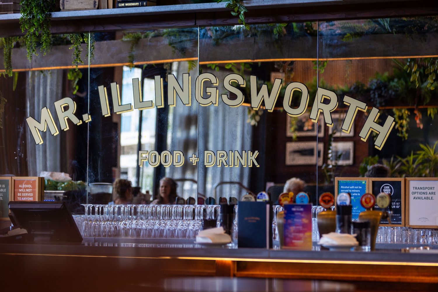 A cozy bar interior with illuminated glass bottles and glassware displayed on wooden shelves behind the counter.
