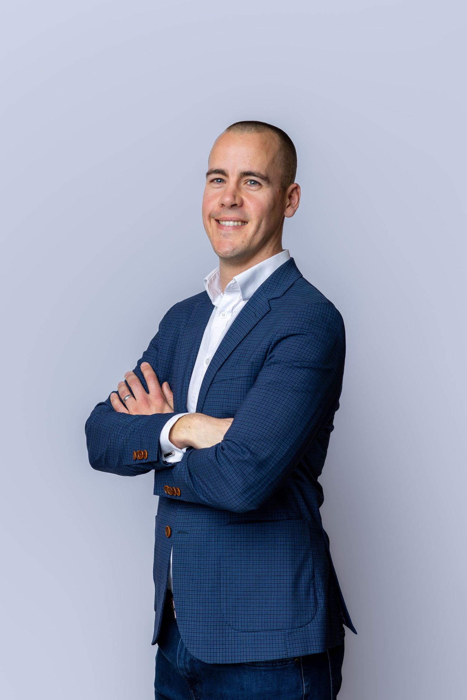 Professional man in blue blazer smiling with arms crossed against gray background.