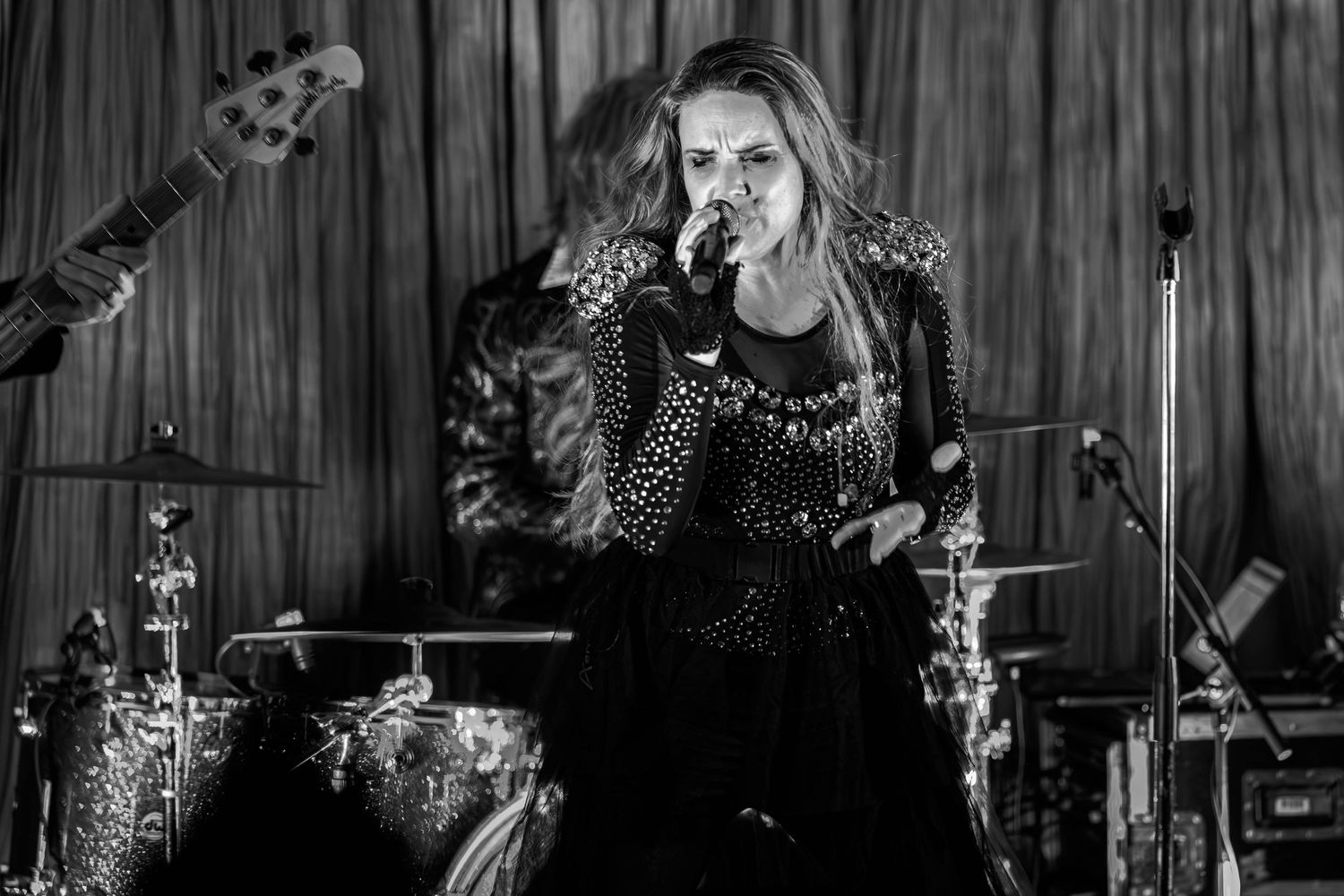 Female rock singer performing on stage in black studded outfit, singing into microphone in black and white photo.