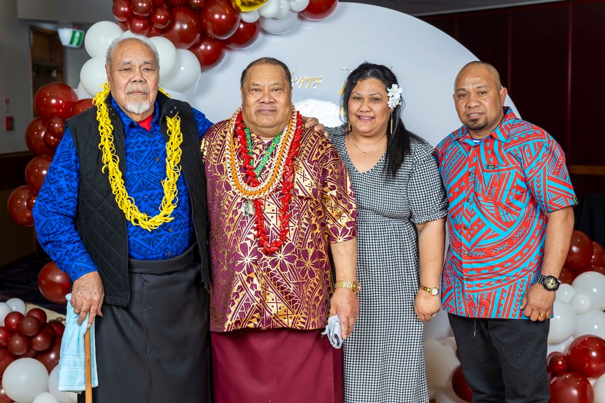 People wearing colorful Hawaiian leis and traditional Pacific Islander clothing pose together at a festive celebration.