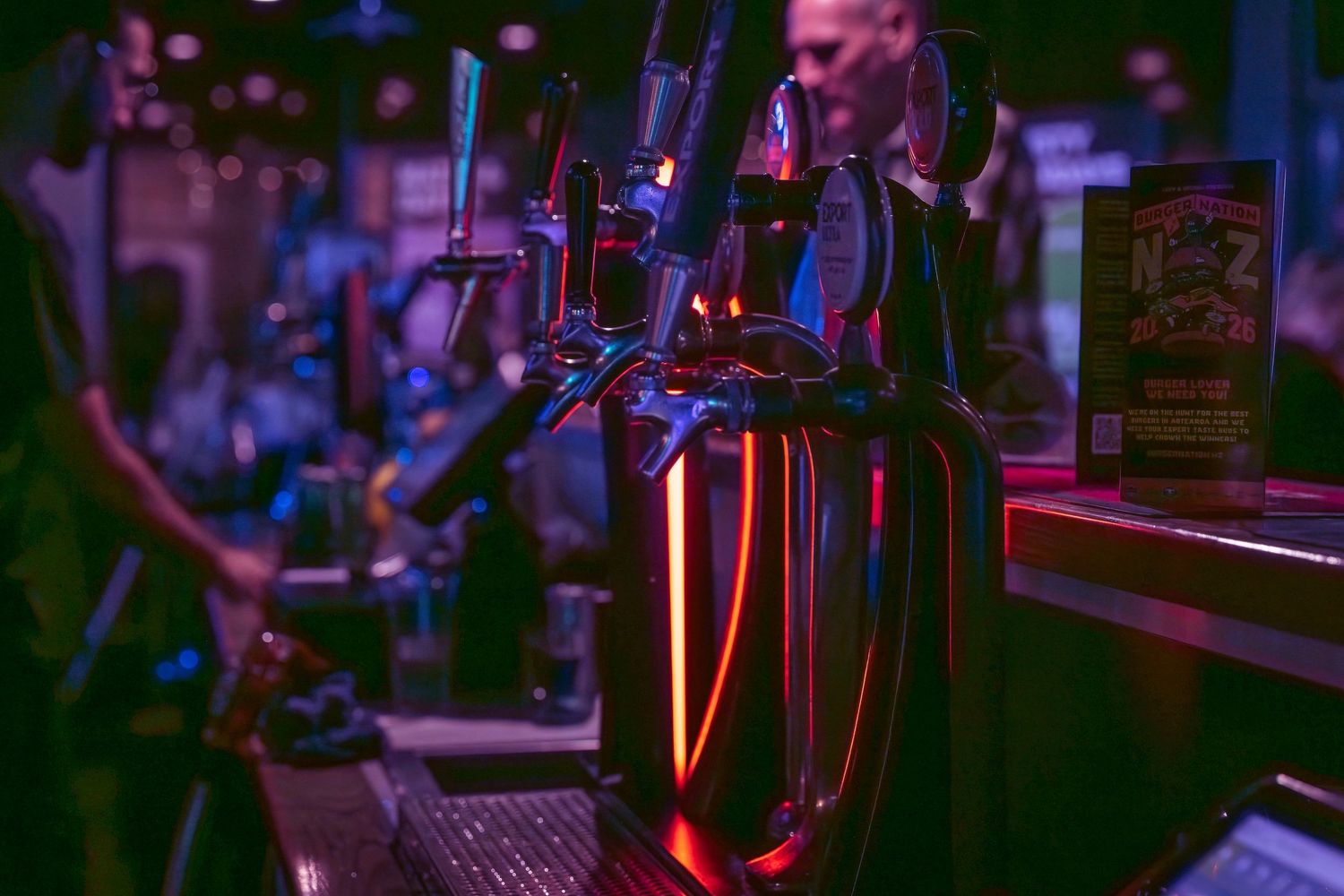 Illuminated beer taps and bar equipment in a dimly lit pub with purple and blue ambient lighting.