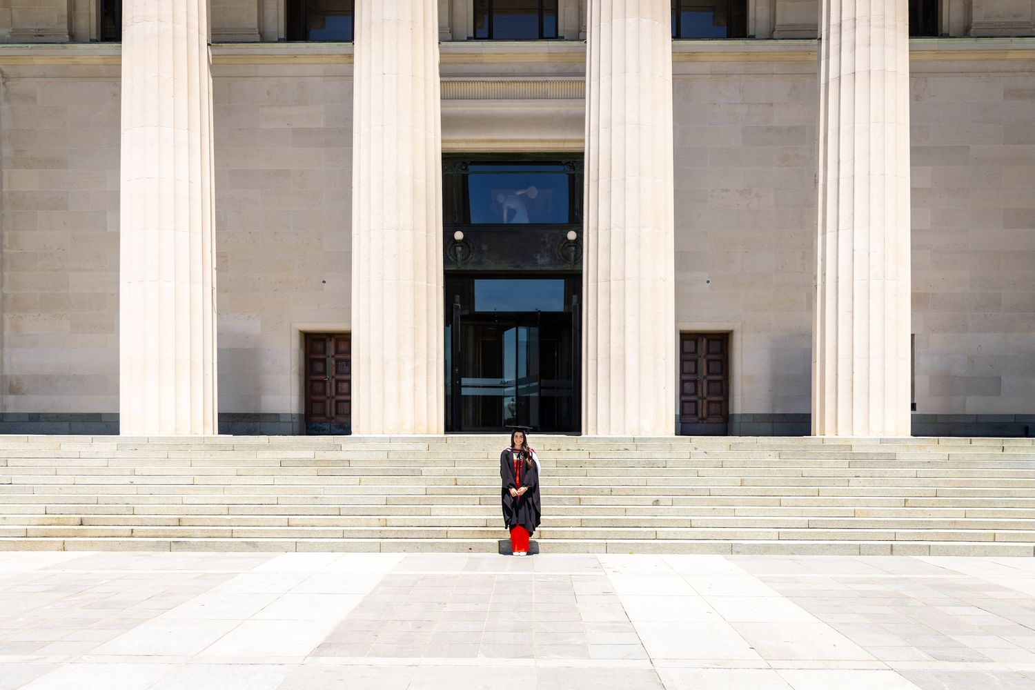 A guard in ceremonial uniform stands before a neoclassical building with tall columns and wide stone steps.