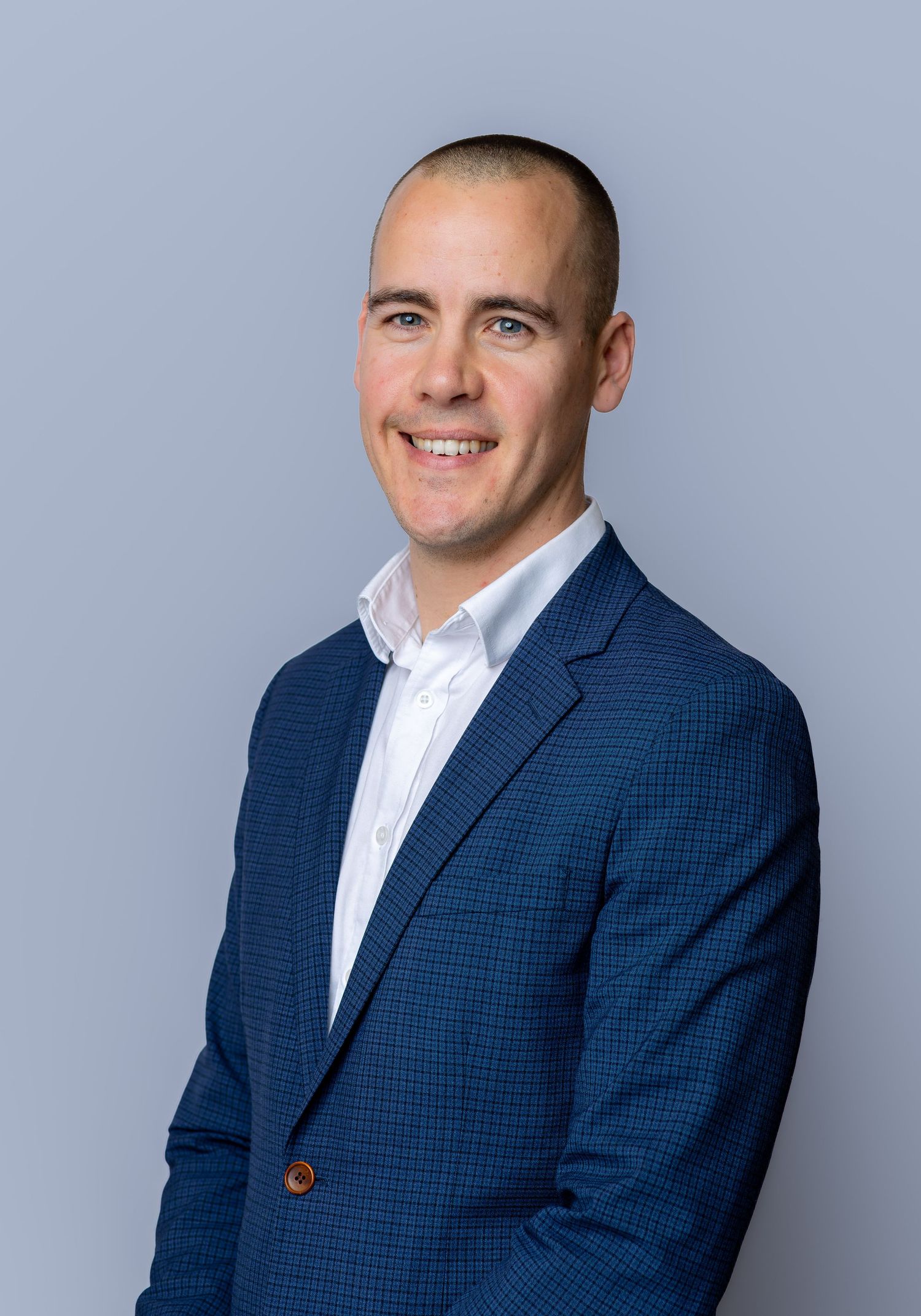 Professional man in blue blazer and white shirt smiling confidently against a gray background.