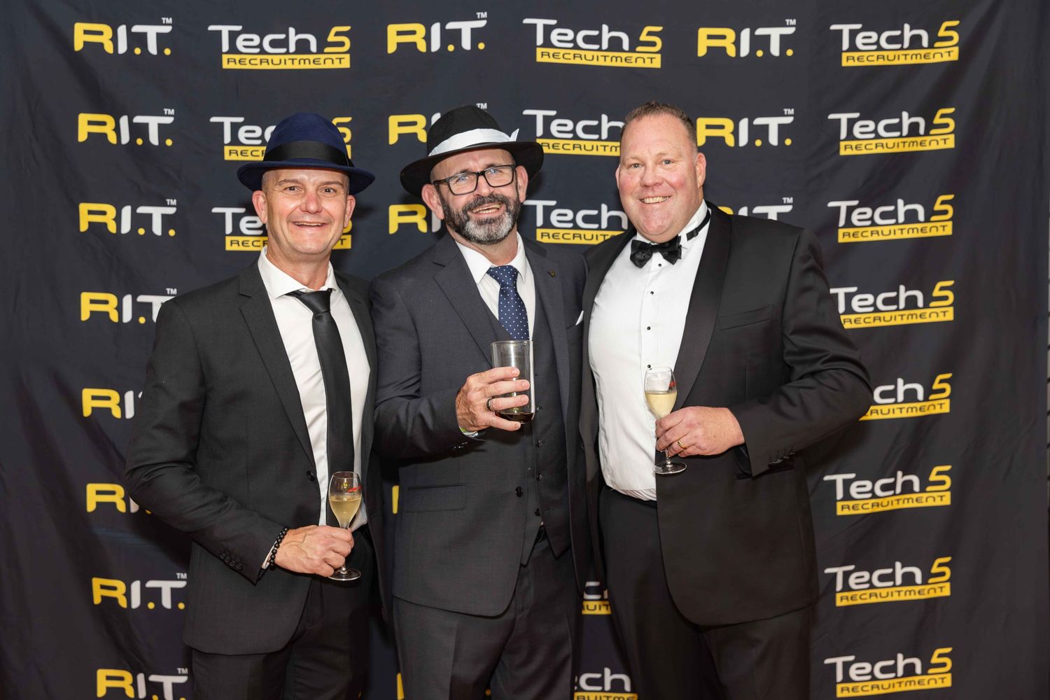 Three men in formal attire pose together at RIT Tech 5 awards event backdrop.