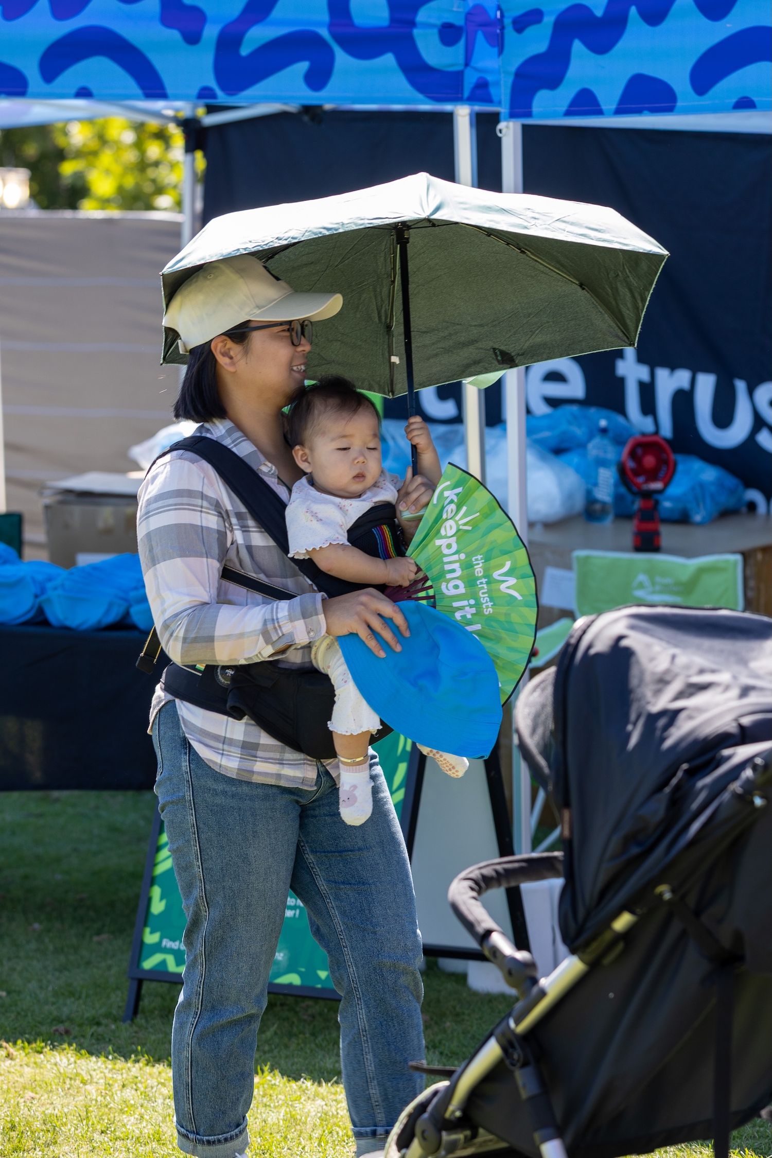 People with strollers gather at an outdoor event under white umbrellas and tents.