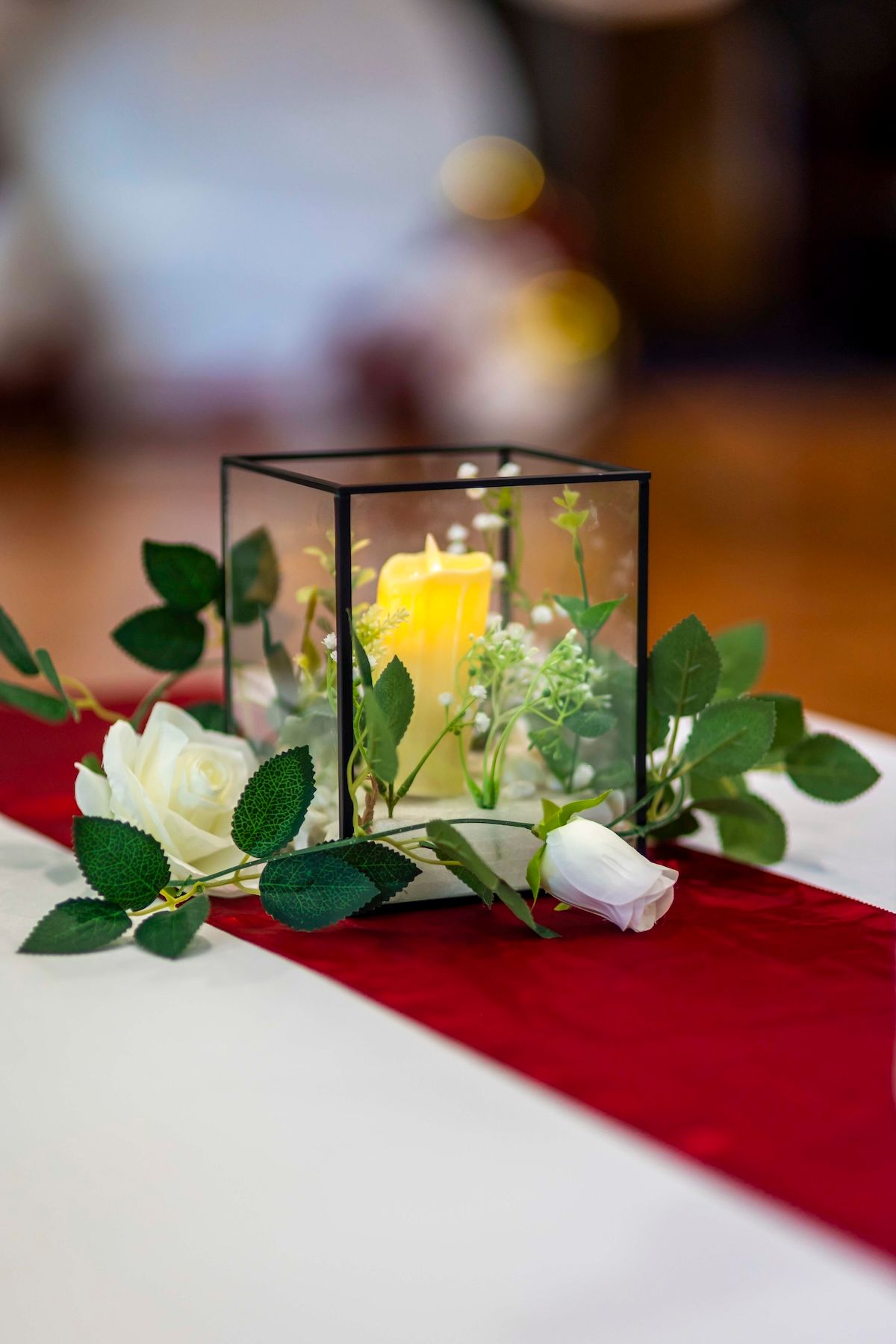 Glass terrarium centerpiece with white flowers and green foliage arranged on red and white table linens.