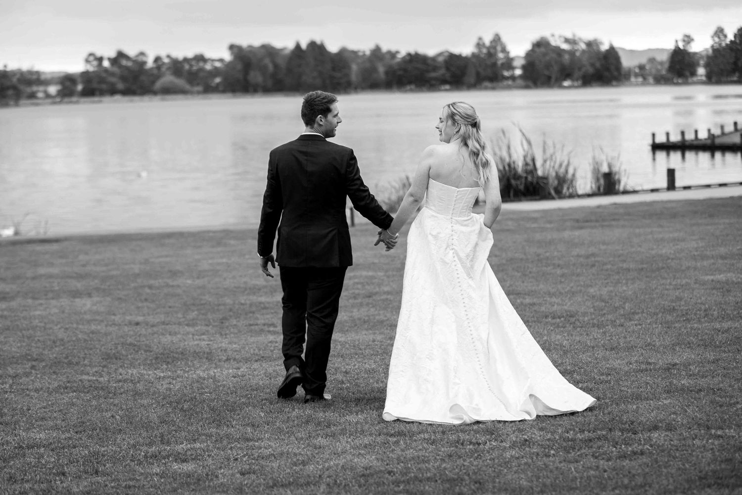 Black and white wedding photo of couple walking by a lake.