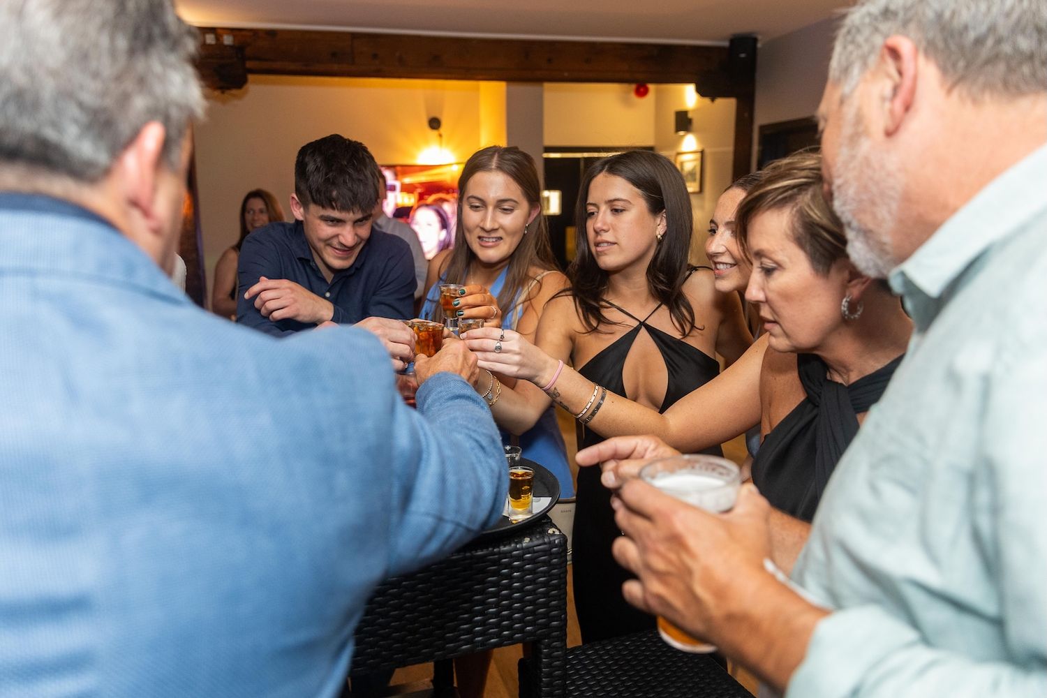 Group of friends toasting with drinks at a casual indoor gathering, smiling and celebrating together.