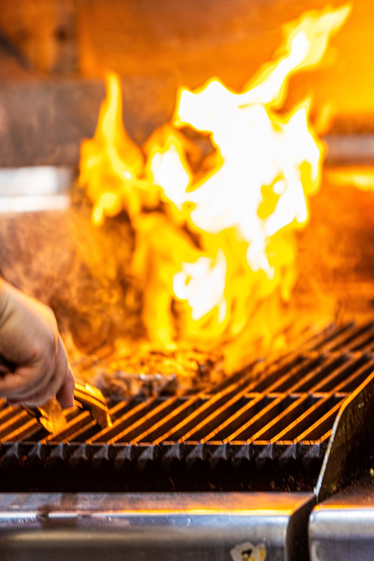 Flames rise dramatically from a hot grill grate during intense barbecue cooking at high temperature.