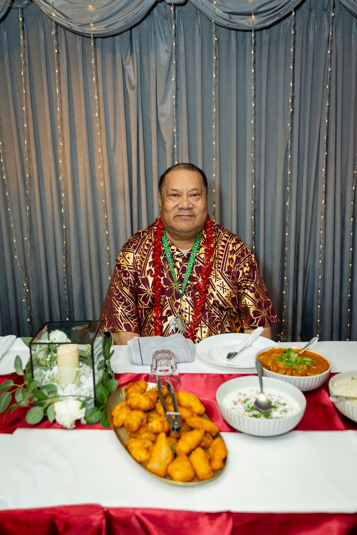 Traditional Polynesian feast table decorated with fresh fruits, leis, and blue curtain backdrop at formal celebration.