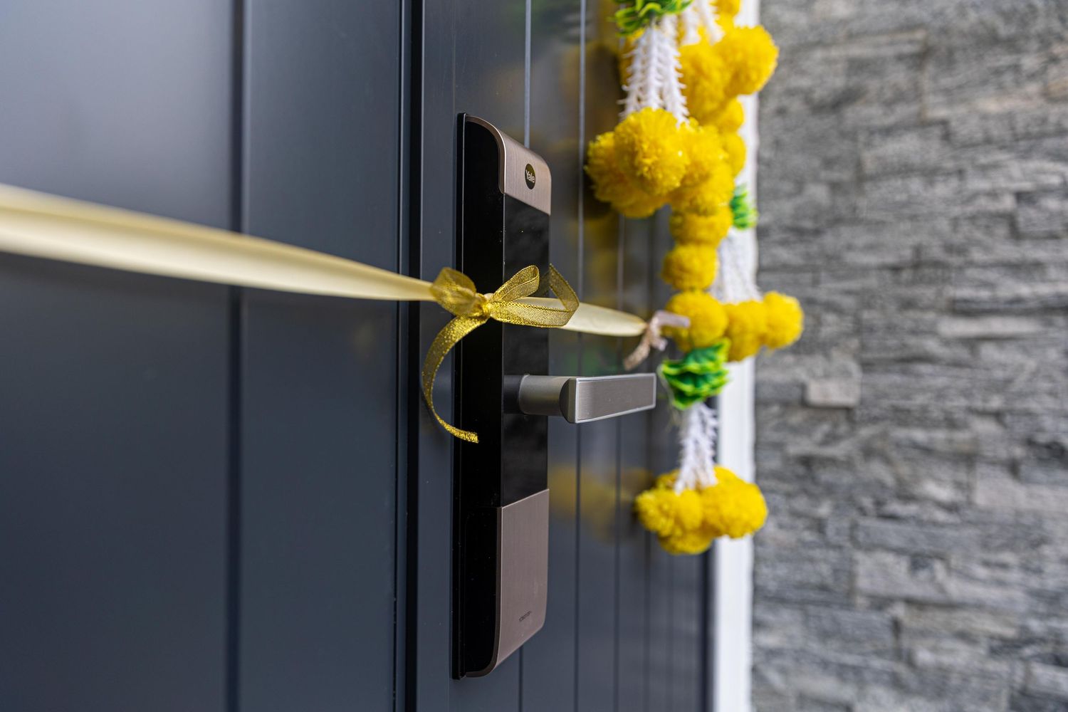 Modern dark door handle adorned with yellow ribbon bow and decorative floral garland for a festive housewarming.