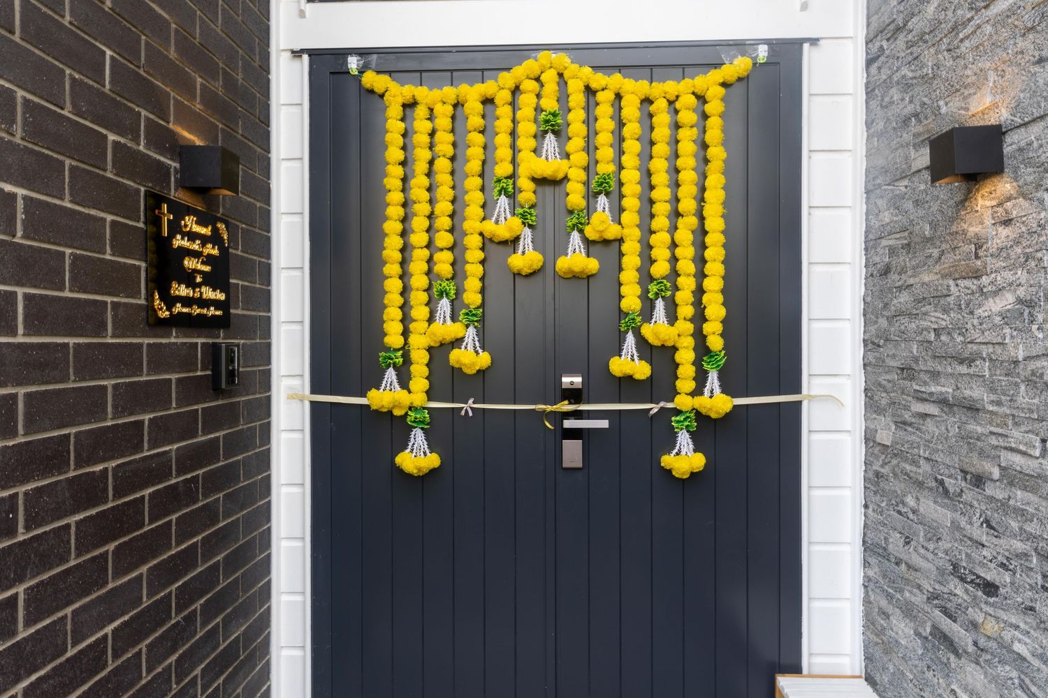 Dark grey front door decorated with vibrant yellow marigold garlands and tassels for a festive Indian celebration.
