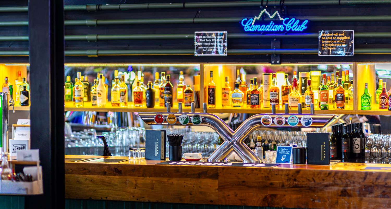 Illuminated bar shelves display colorful bottles of liquor and spirits against dark ambient lighting in a modern establishment.