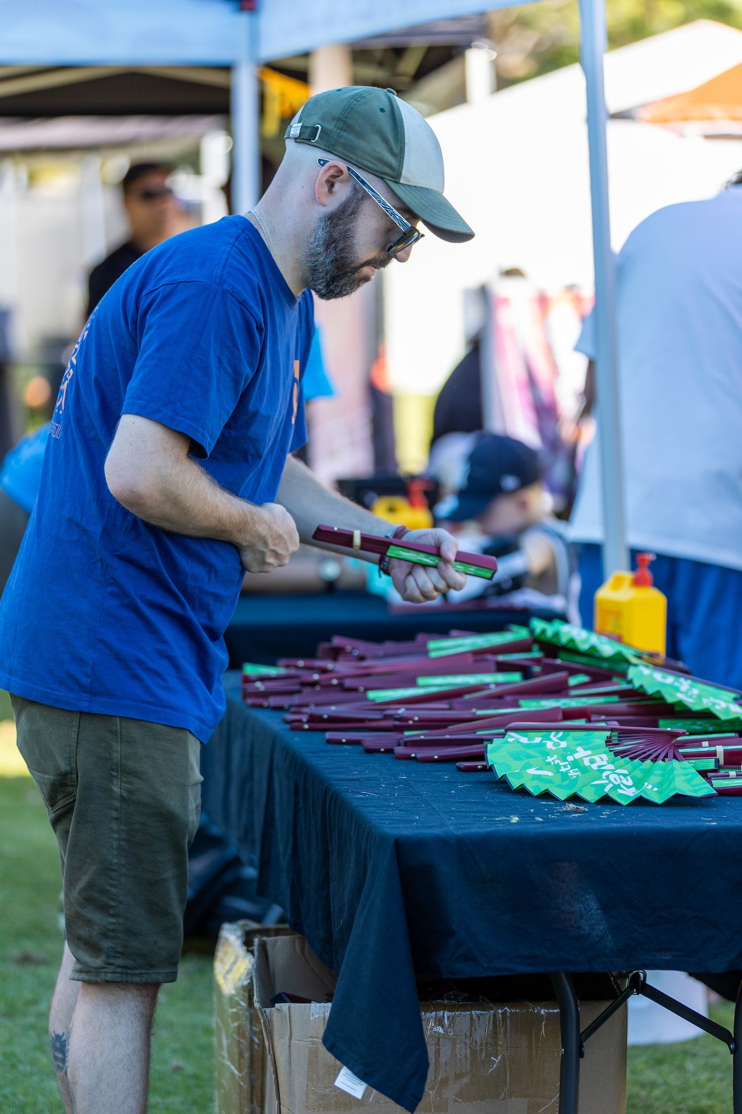 Event staff organizing merchandise on display tables at an outdoor festival.
