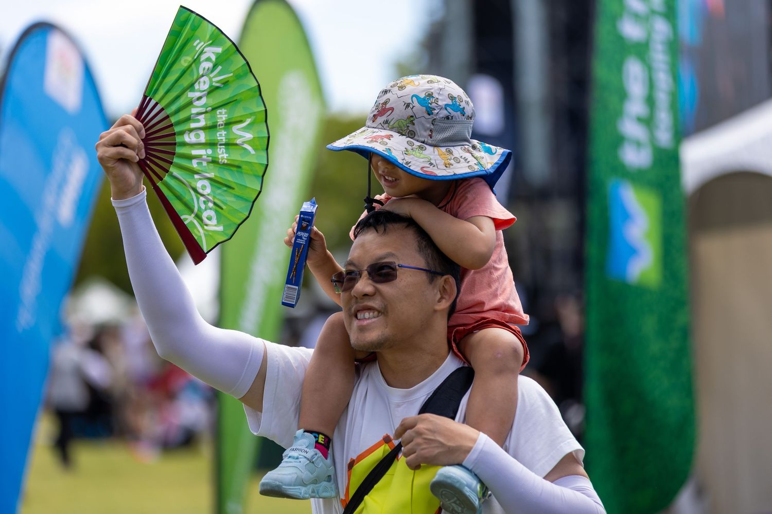 People hold up decorative green and white folding fans at outdoor gathering.