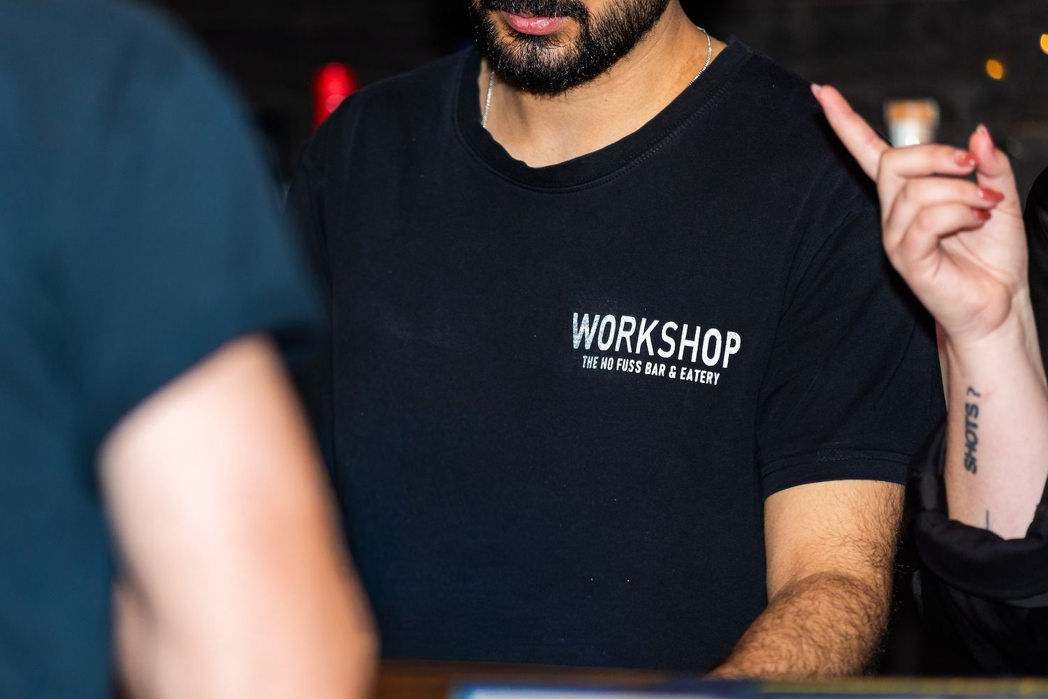 Close-up shot of someone wearing a black Workshop branded t-shirt in dim lighting.